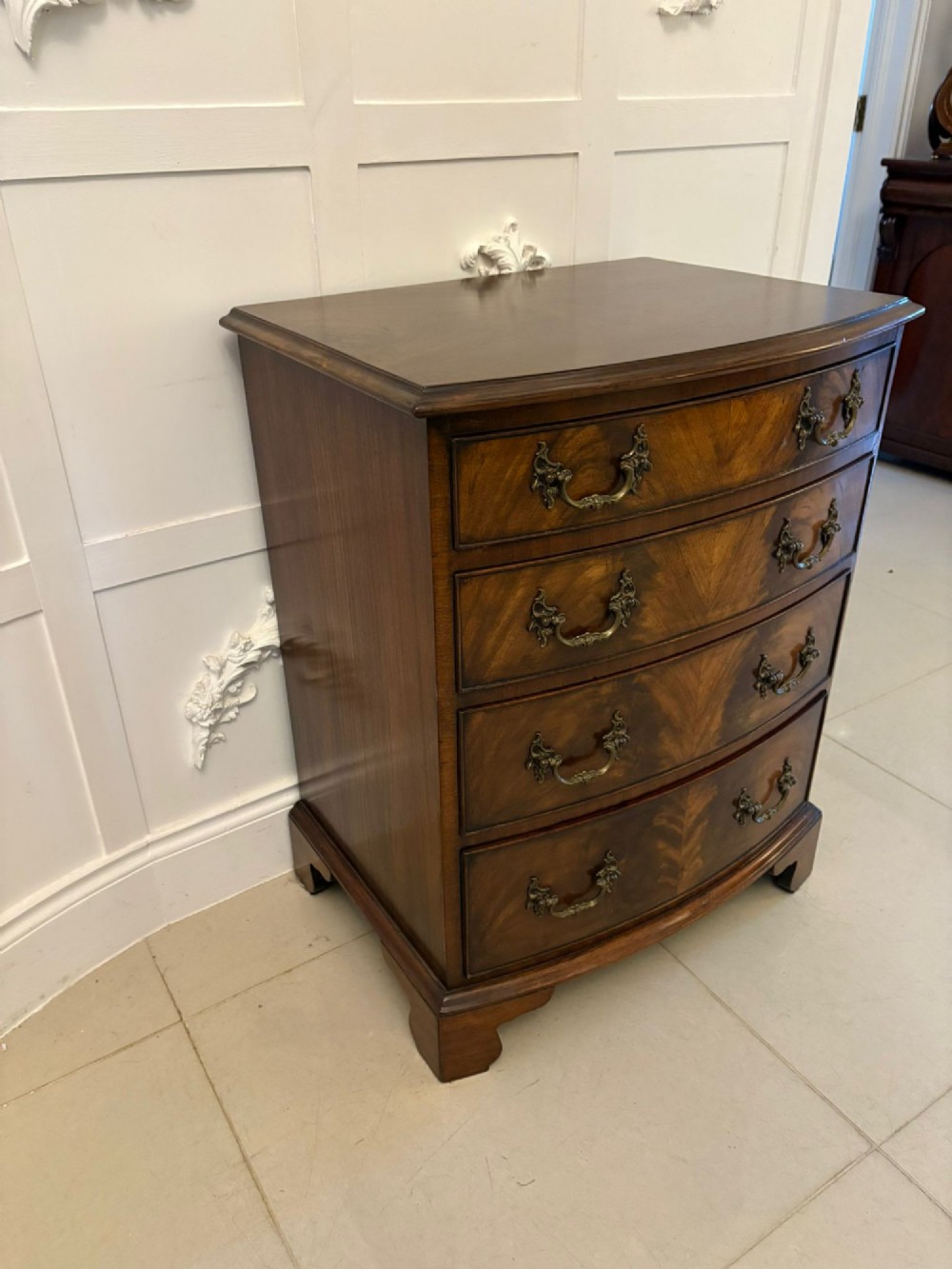 An Edwardian bow-fronted mahogany chest with four drawers, decorative brass handles, and flame veneer drawer fronts set on bracket feet. View II