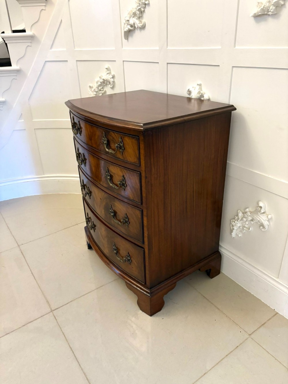 An Edwardian bow-fronted mahogany chest with four drawers, decorative brass handles, and flame veneer drawer fronts set on bracket feet. View IV