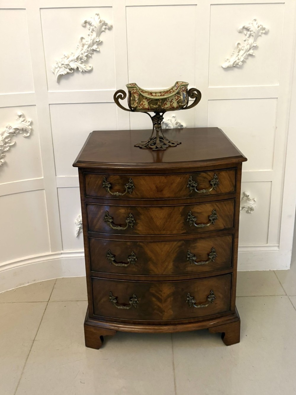An Edwardian bow-fronted mahogany chest with four drawers, decorative brass handles, and flame veneer drawer fronts set on bracket feet. View V
