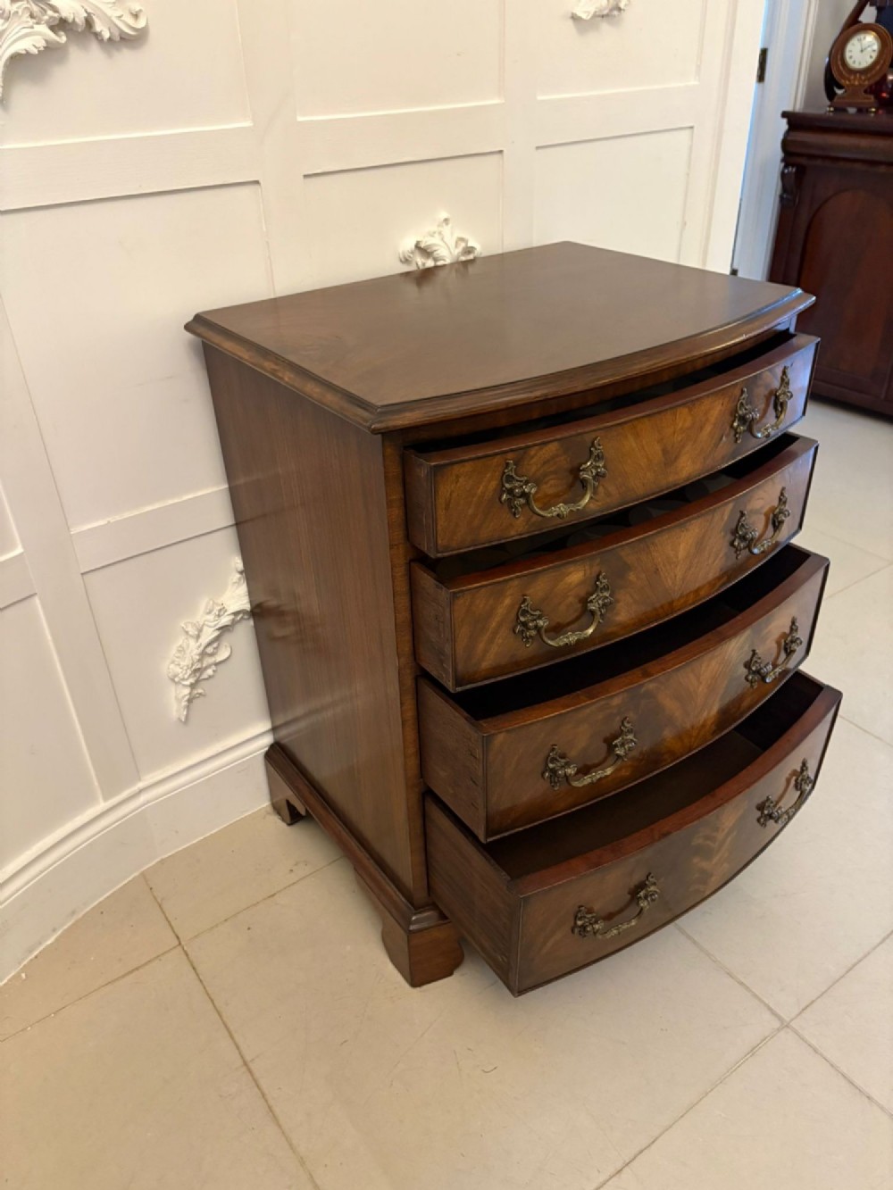 An Edwardian bow-fronted mahogany chest with four drawers, decorative brass handles, and flame veneer drawer fronts set on bracket feet. View VI