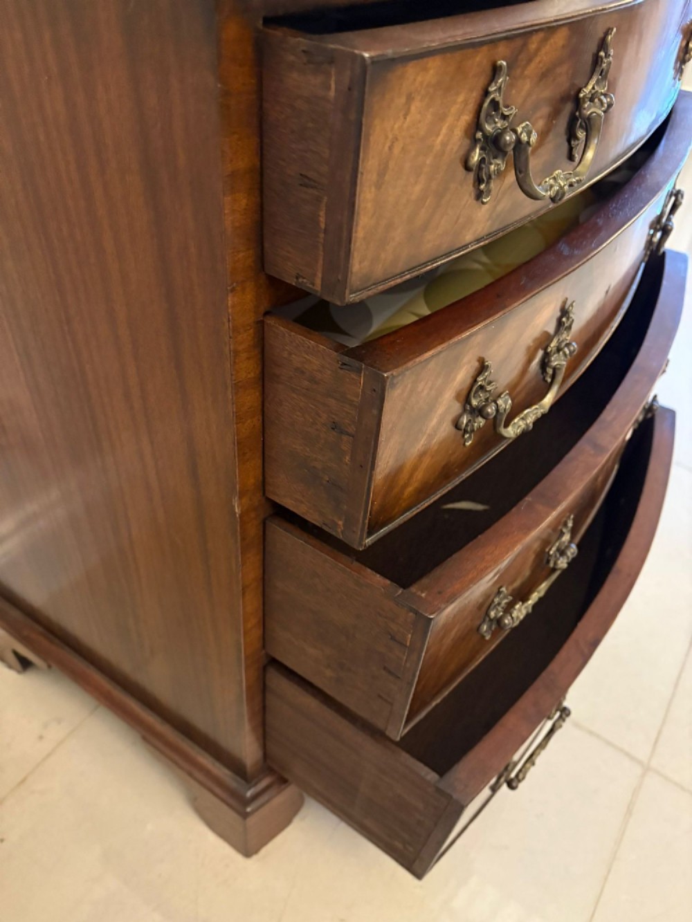 An Edwardian bow-fronted mahogany chest with four drawers, decorative brass handles, and flame veneer drawer fronts set on bracket feet. View VII