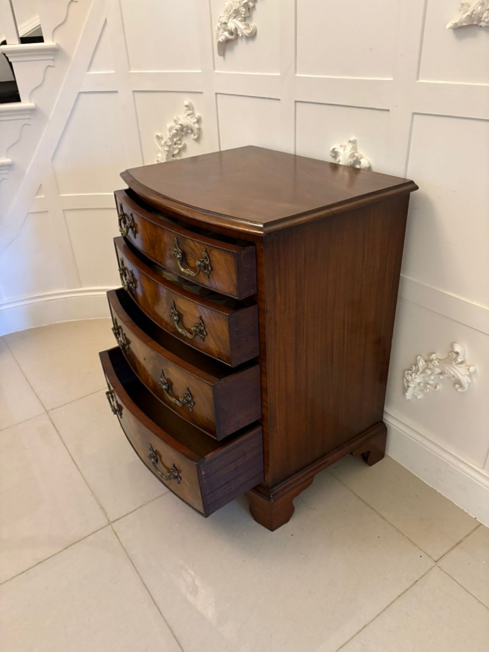 An Edwardian bow-fronted mahogany chest with four drawers, decorative brass handles, and flame veneer drawer fronts set on bracket feet. View VIII