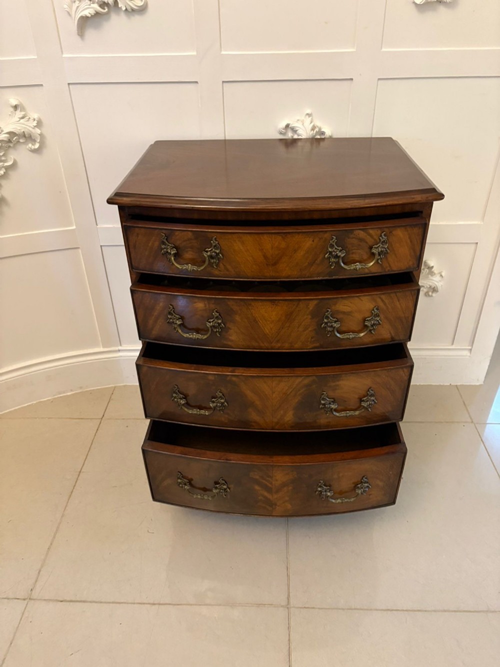 An Edwardian bow-fronted mahogany chest with four drawers, decorative brass handles, and flame veneer drawer fronts set on bracket feet. View IX