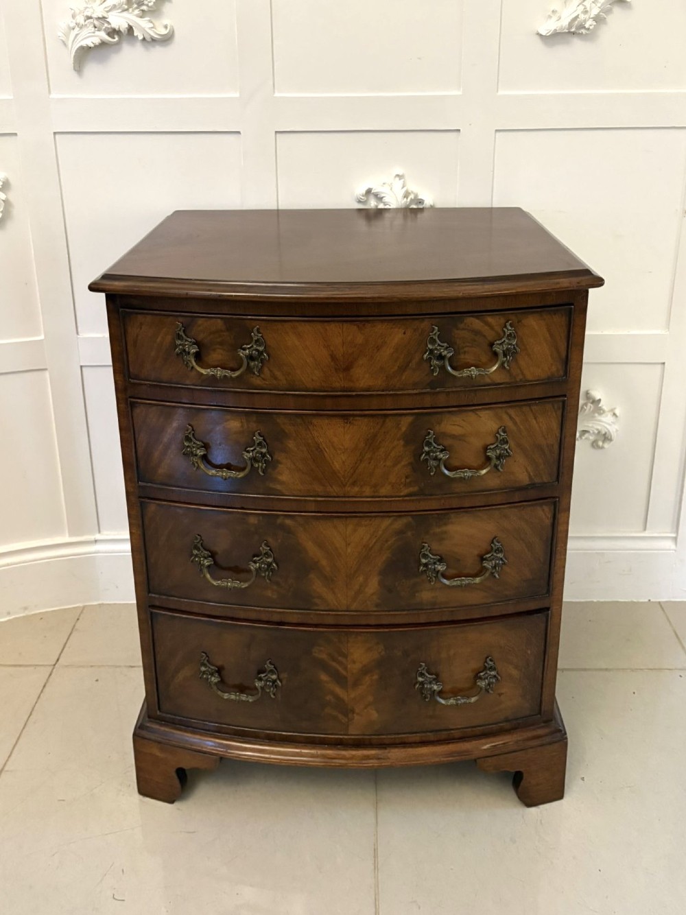 An Edwardian bow-fronted mahogany chest with four drawers, decorative brass handles, and flame veneer drawer fronts set on bracket feet.