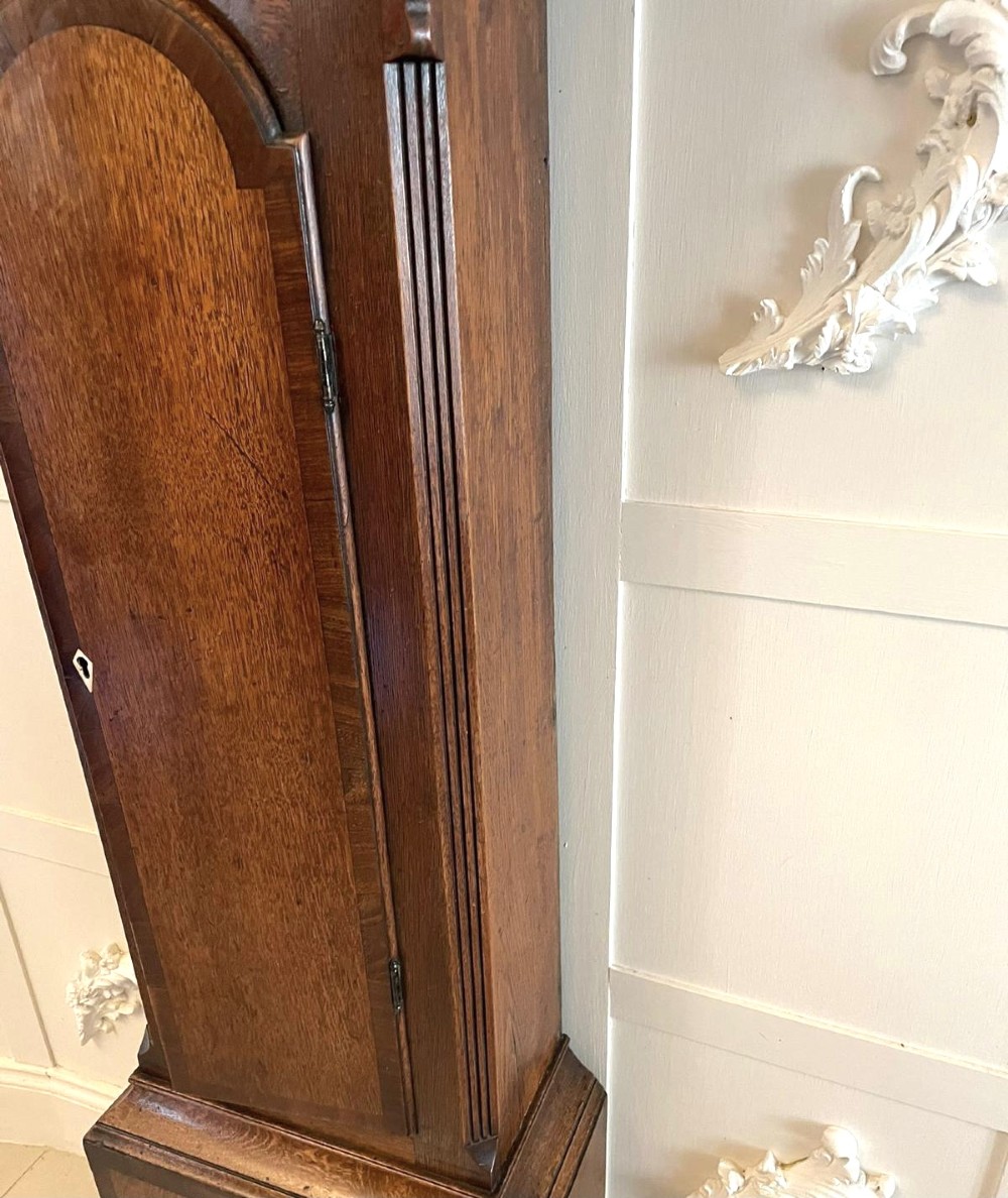 A George III oak longcase clock featuring an etched brass dial with silvered chapter ring, inlaid wood motif pediment, and an arched trunk door. View II