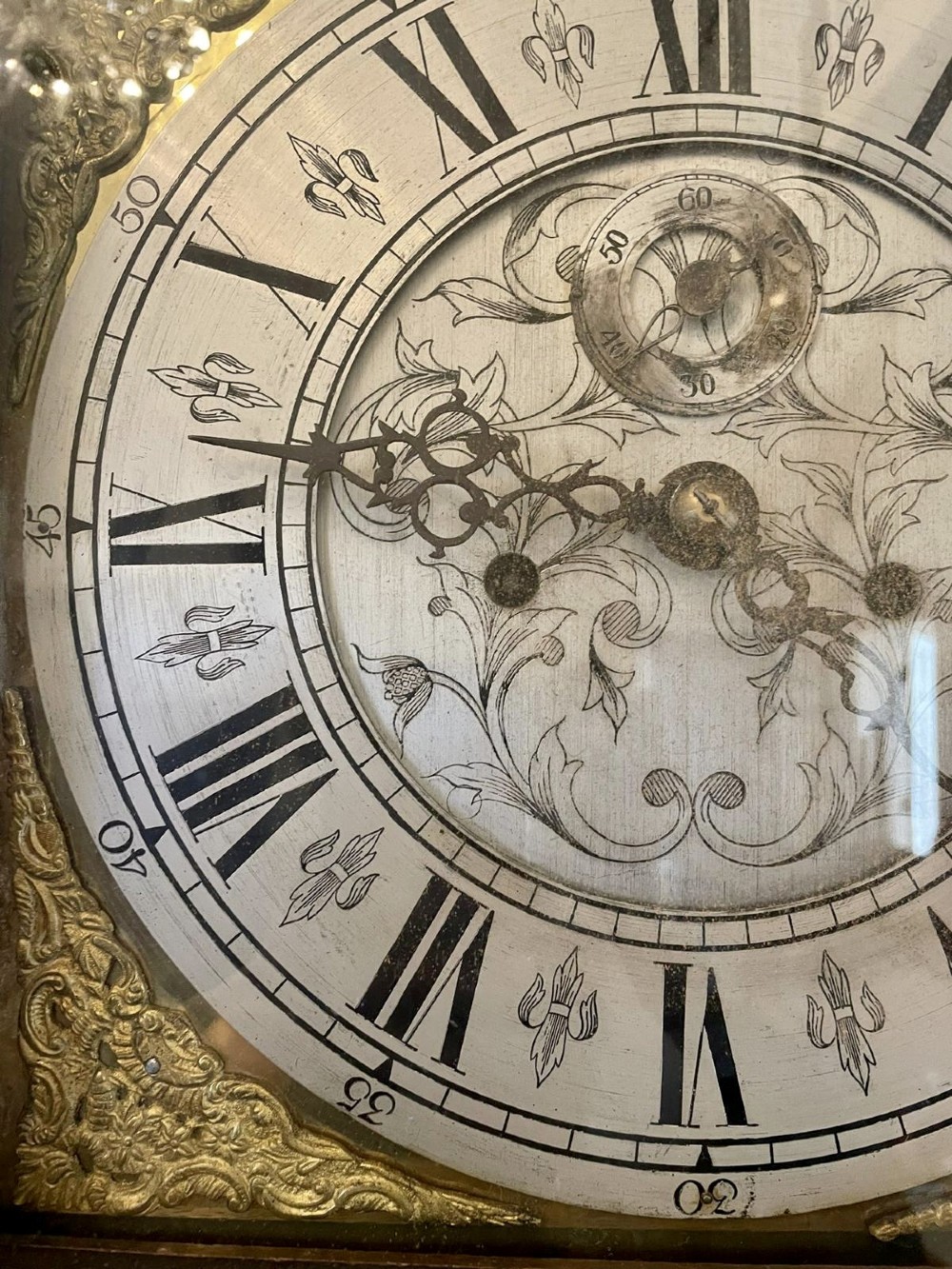 A George III oak longcase clock featuring an etched brass dial with silvered chapter ring, inlaid wood motif pediment, and an arched trunk door. View V