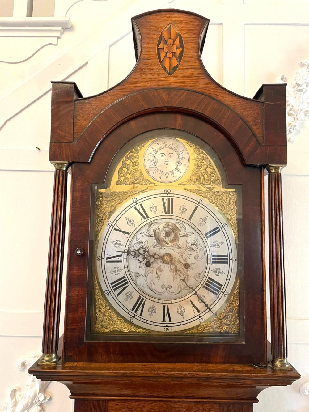 A George III oak longcase clock featuring an etched brass dial with silvered chapter ring, inlaid wood motif pediment, and an arched trunk door. View XII