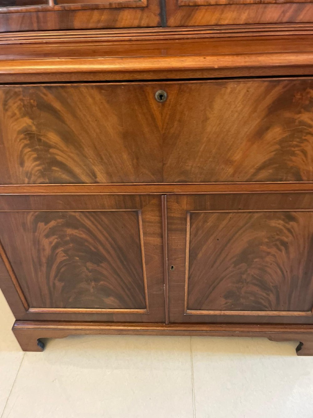 An antique Regency mahogany secretaire bookcase featuring a top scroll pediment, glazed upper doors with astragal moulding, and a lower double cupboard. View IV