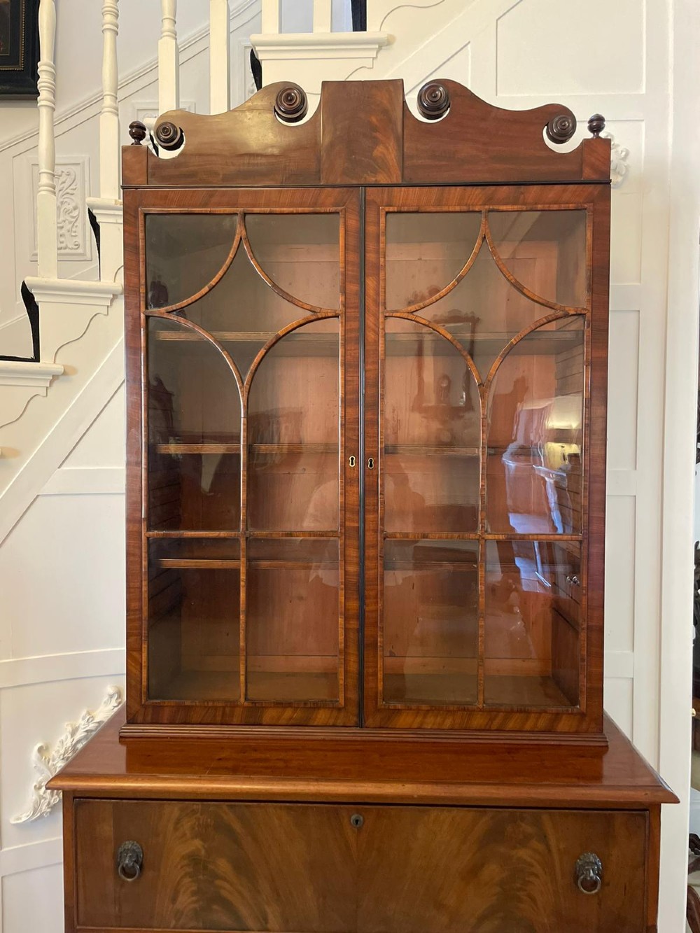 An antique Regency mahogany secretaire bookcase featuring a top scroll pediment, glazed upper doors with astragal moulding, and a lower double cupboard. View V