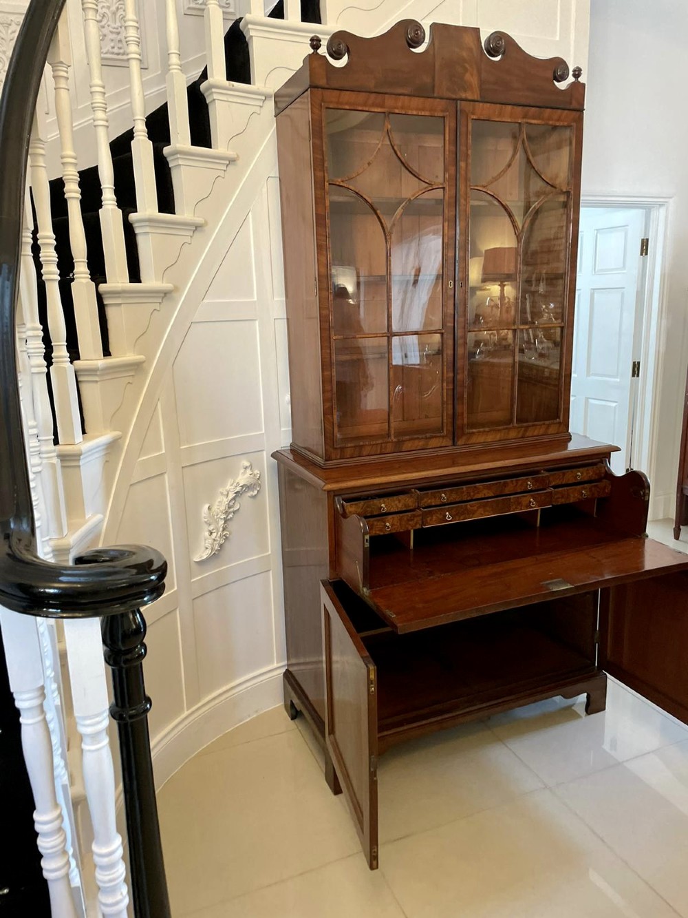 An antique Regency mahogany secretaire bookcase featuring a top scroll pediment, glazed upper doors with astragal moulding, and a lower double cupboard. View XII
