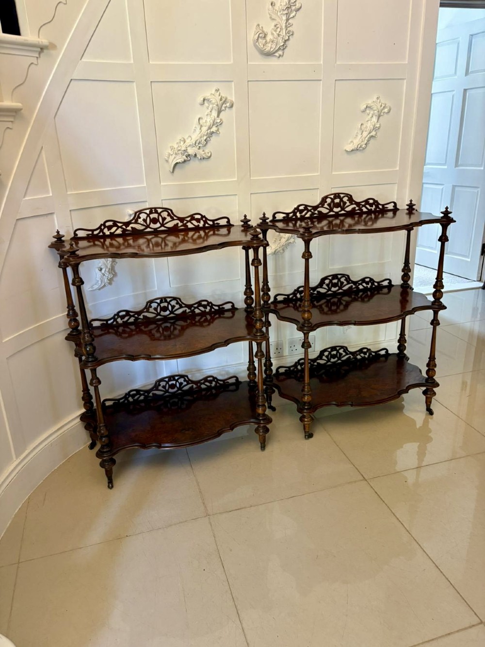 A pair of Victorian burr walnut three-tier whatnots featuring pierced fretwork galleries, serpentine fronts, and turned upright supports on castors. View VI