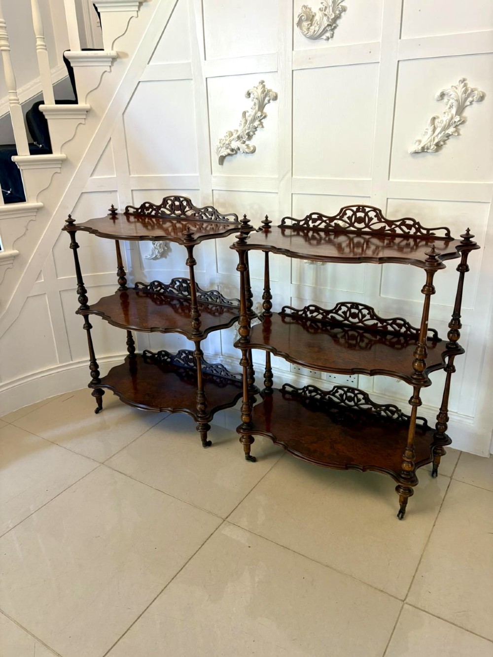 A pair of Victorian burr walnut three-tier whatnots featuring pierced fretwork galleries, serpentine fronts, and turned upright supports on castors. View X