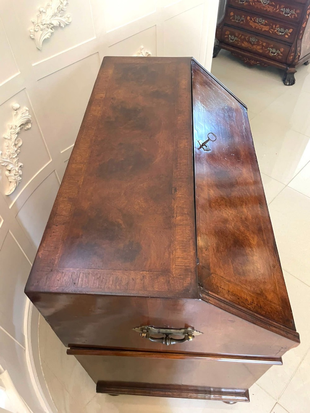 An antique burr walnut slant-front bureau featuring herringbone inlay, brass hardware, three lower drawers, and turned bun feet. View VI