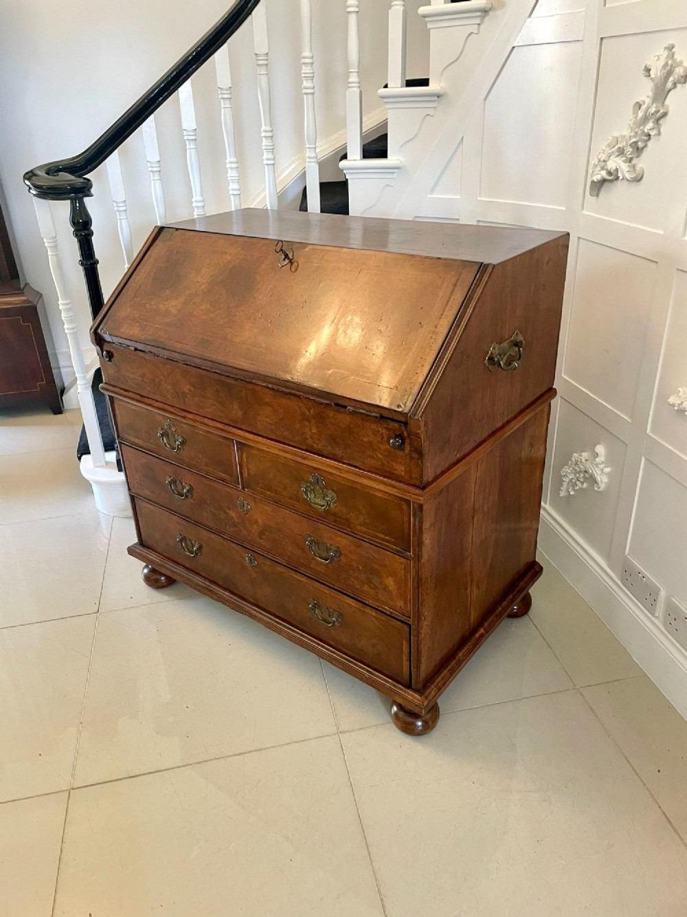 An antique burr walnut slant-front bureau featuring herringbone inlay, brass hardware, three lower drawers, and turned bun feet. View XIV