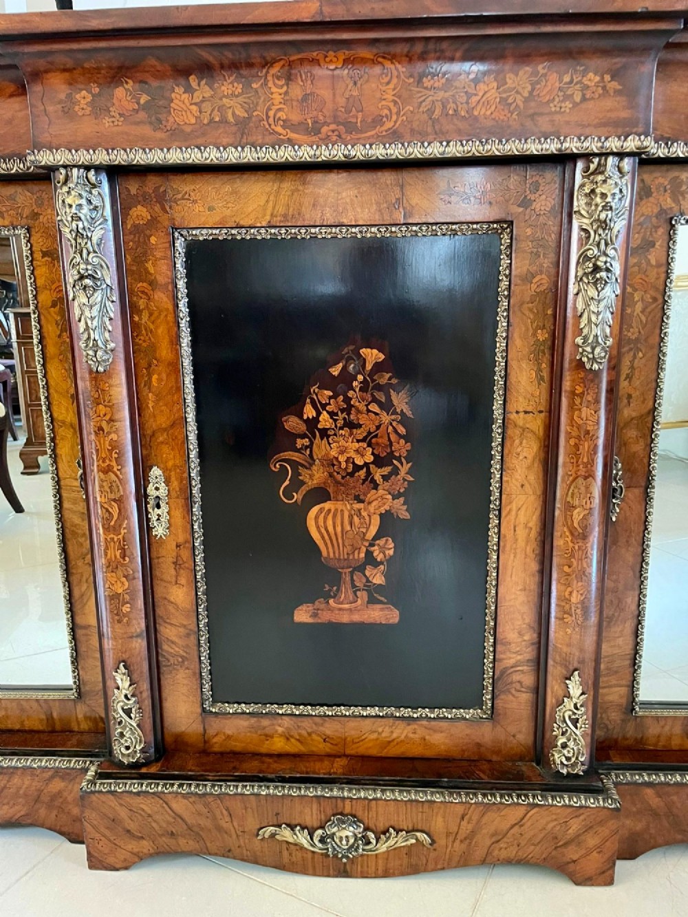 A Victorian burr walnut breakfront credenza featuring brass mounts, a central floral marquetry panel, and mirrored side doors. View XIV