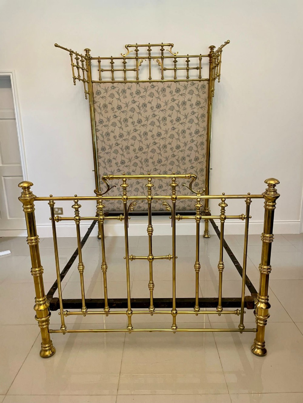 An antique Victorian solid brass half tester double bed featuring turned posts, spindle balusters, cast decorative mounts, and an upholstered floral panel. View II