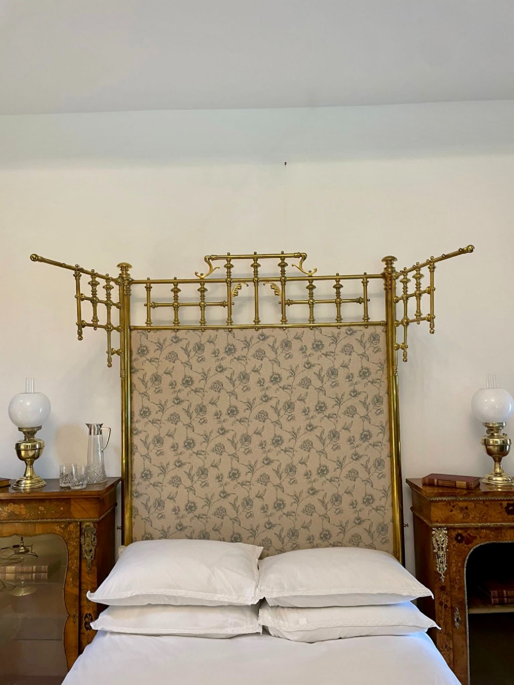 An antique Victorian solid brass half tester double bed featuring turned posts, spindle balusters, cast decorative mounts, and an upholstered floral panel. View IV