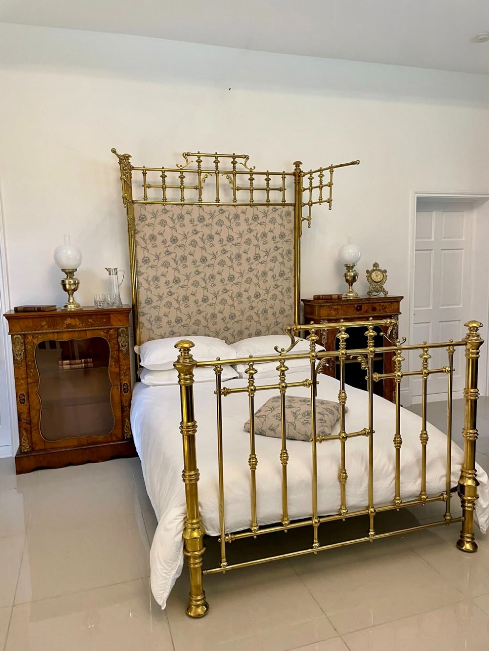 An antique Victorian solid brass half tester double bed featuring turned posts, spindle balusters, cast decorative mounts, and an upholstered floral panel. View V