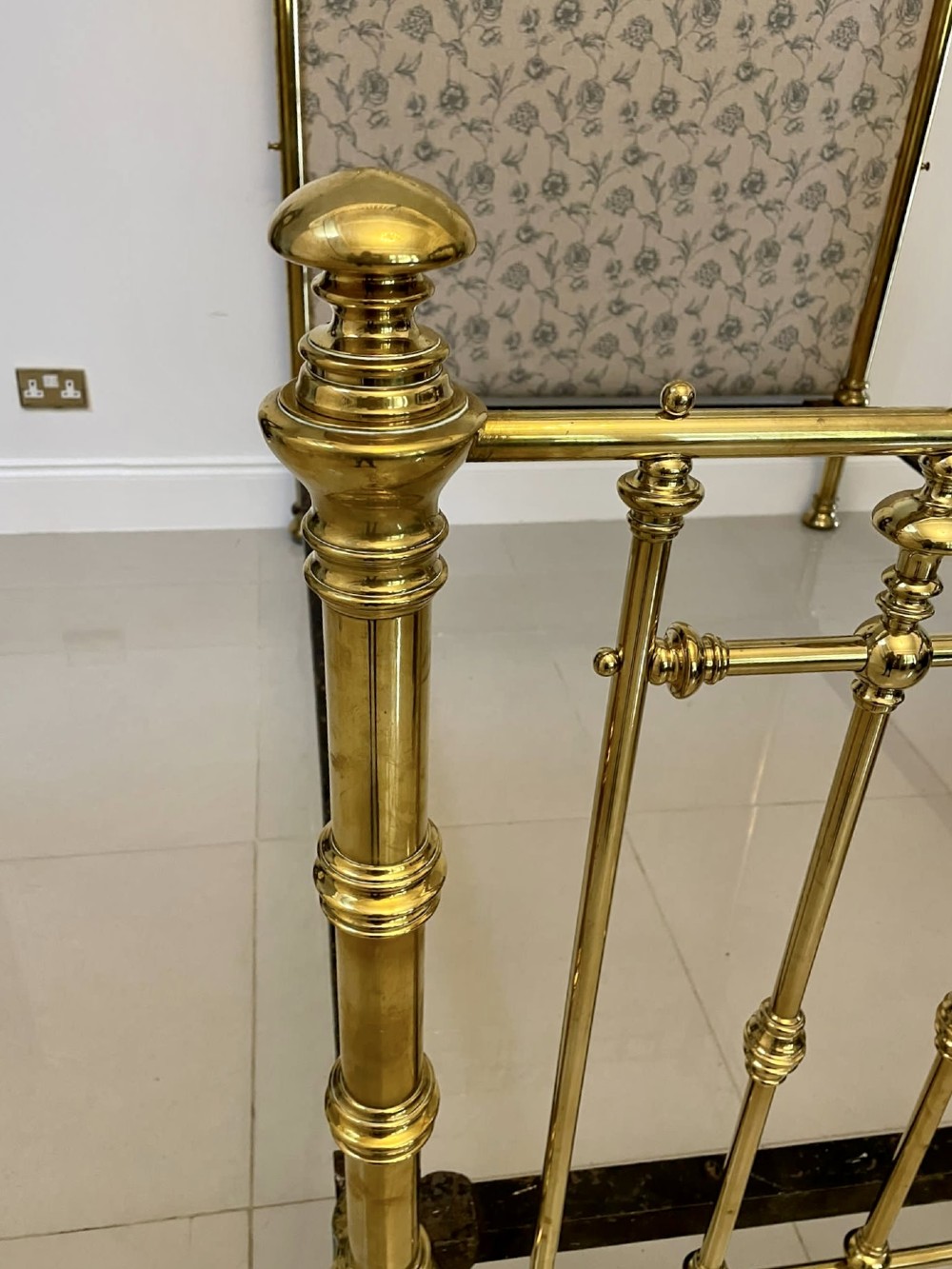 An antique Victorian solid brass half tester double bed featuring turned posts, spindle balusters, cast decorative mounts, and an upholstered floral panel. View VII