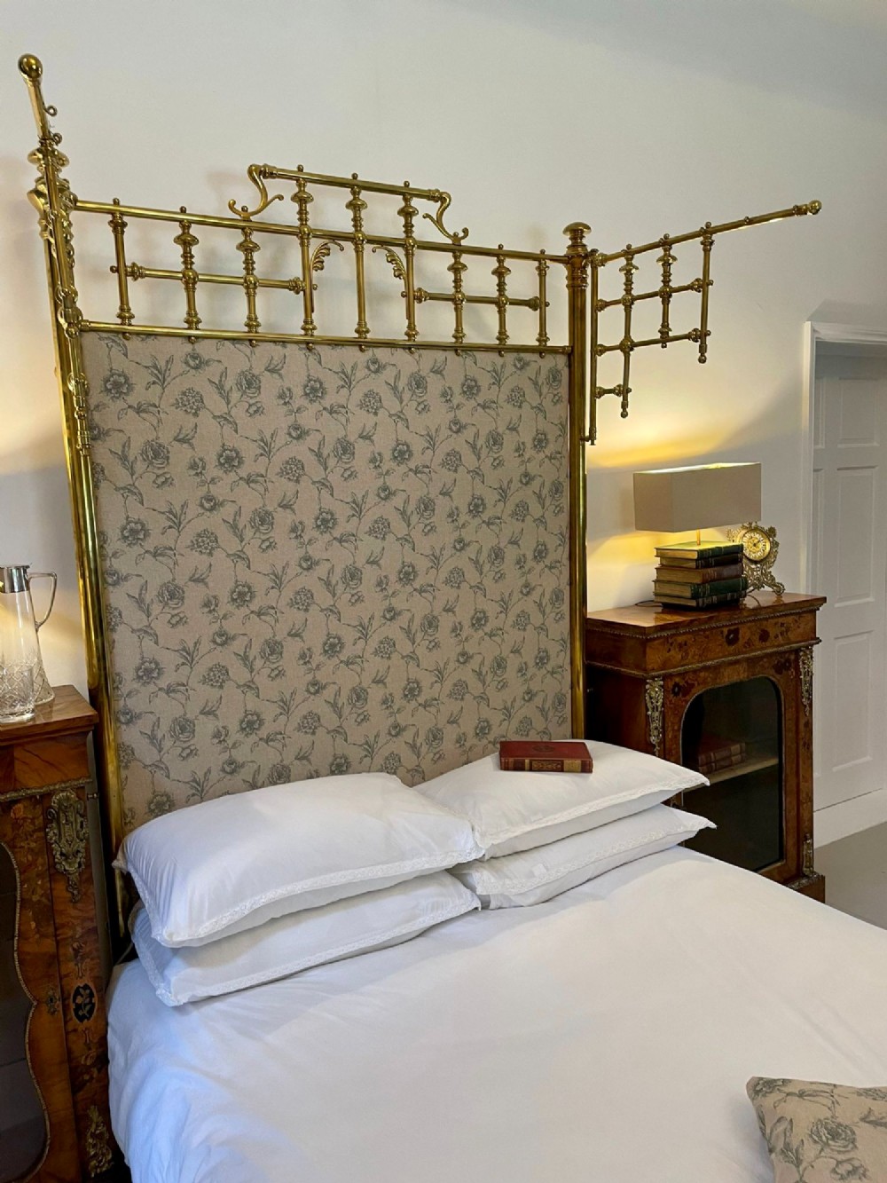 An antique Victorian solid brass half tester double bed featuring turned posts, spindle balusters, cast decorative mounts, and an upholstered floral panel. View IX