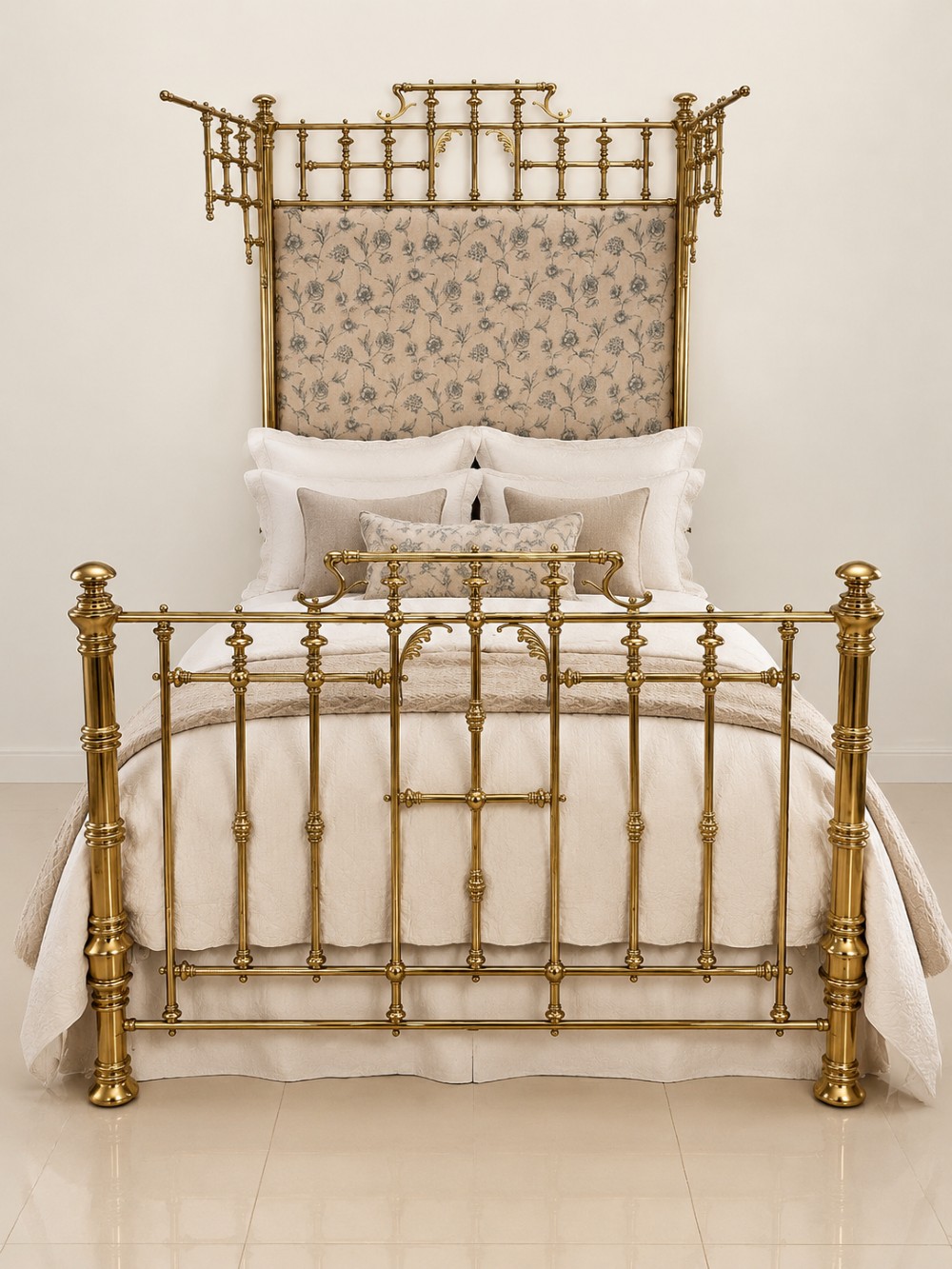 An antique Victorian solid brass half tester double bed featuring turned posts, spindle balusters, cast decorative mounts, and an upholstered floral panel.