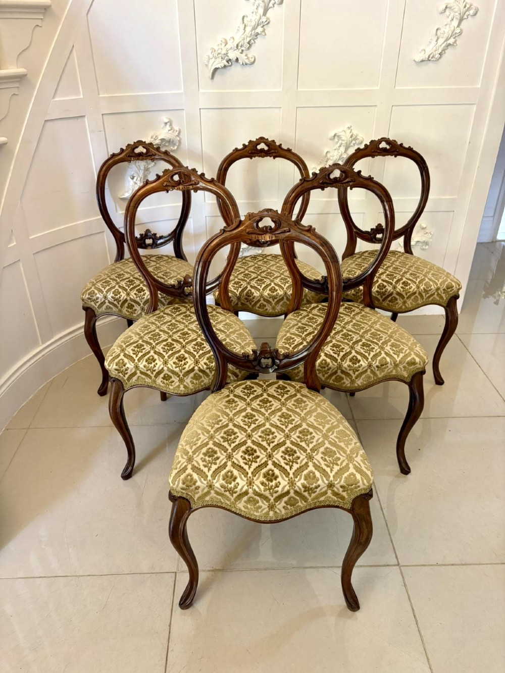 A set of six Victorian carved walnut dining chairs featuring open balloon backs, cabriole legs, and patterned green upholstered seats.