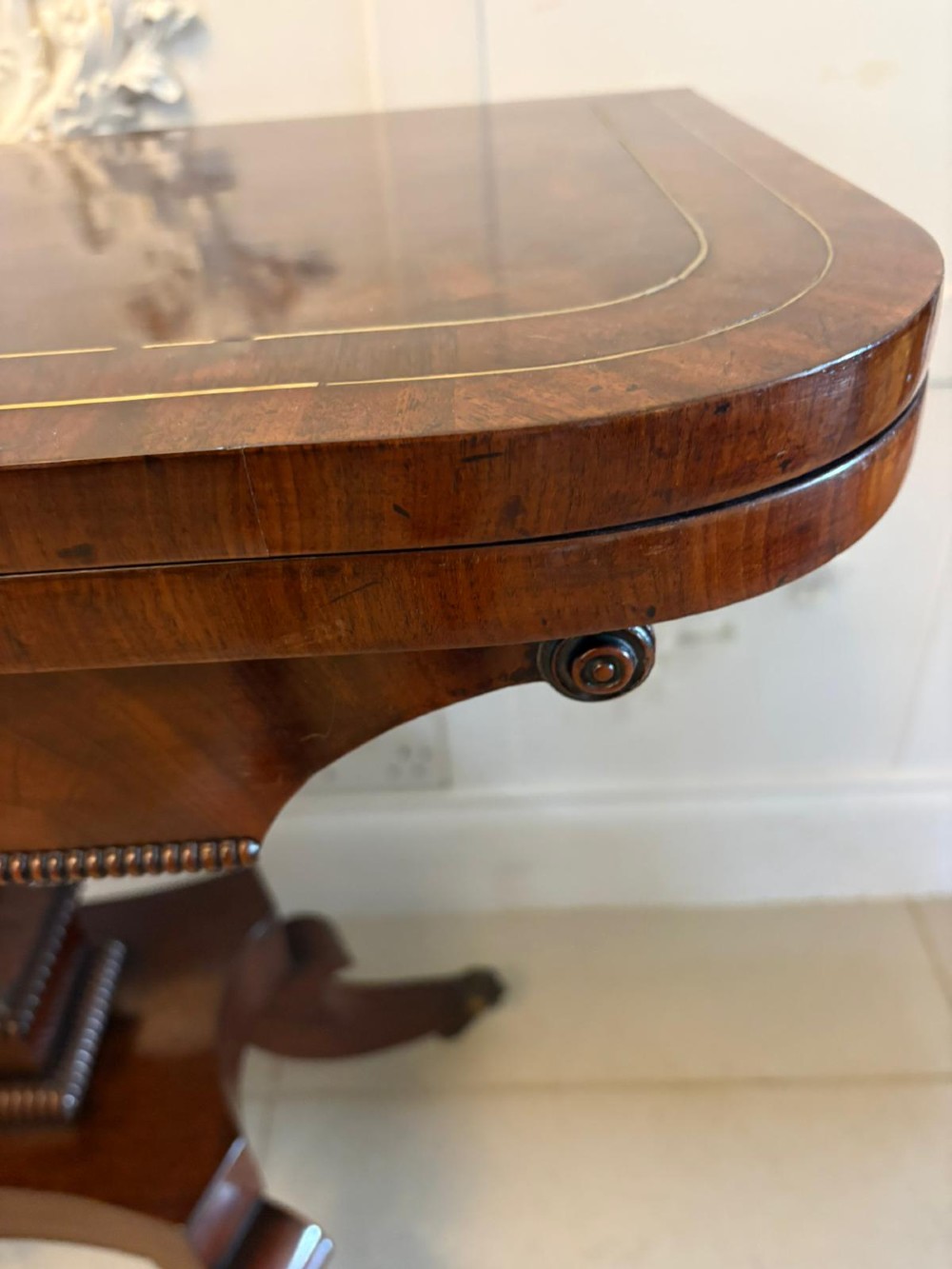 An antique Regency mahogany fold-over card table featuring brass marquetry inlay, a central shaped pedestal, and a splayed base with brass castors. View II