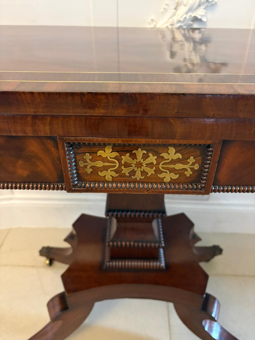 An antique Regency mahogany fold-over card table featuring brass marquetry inlay, a central shaped pedestal, and a splayed base with brass castors. View IV