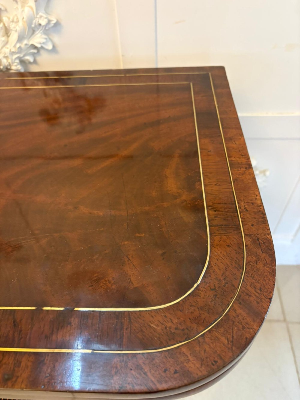 An antique Regency mahogany fold-over card table featuring brass marquetry inlay, a central shaped pedestal, and a splayed base with brass castors. View V