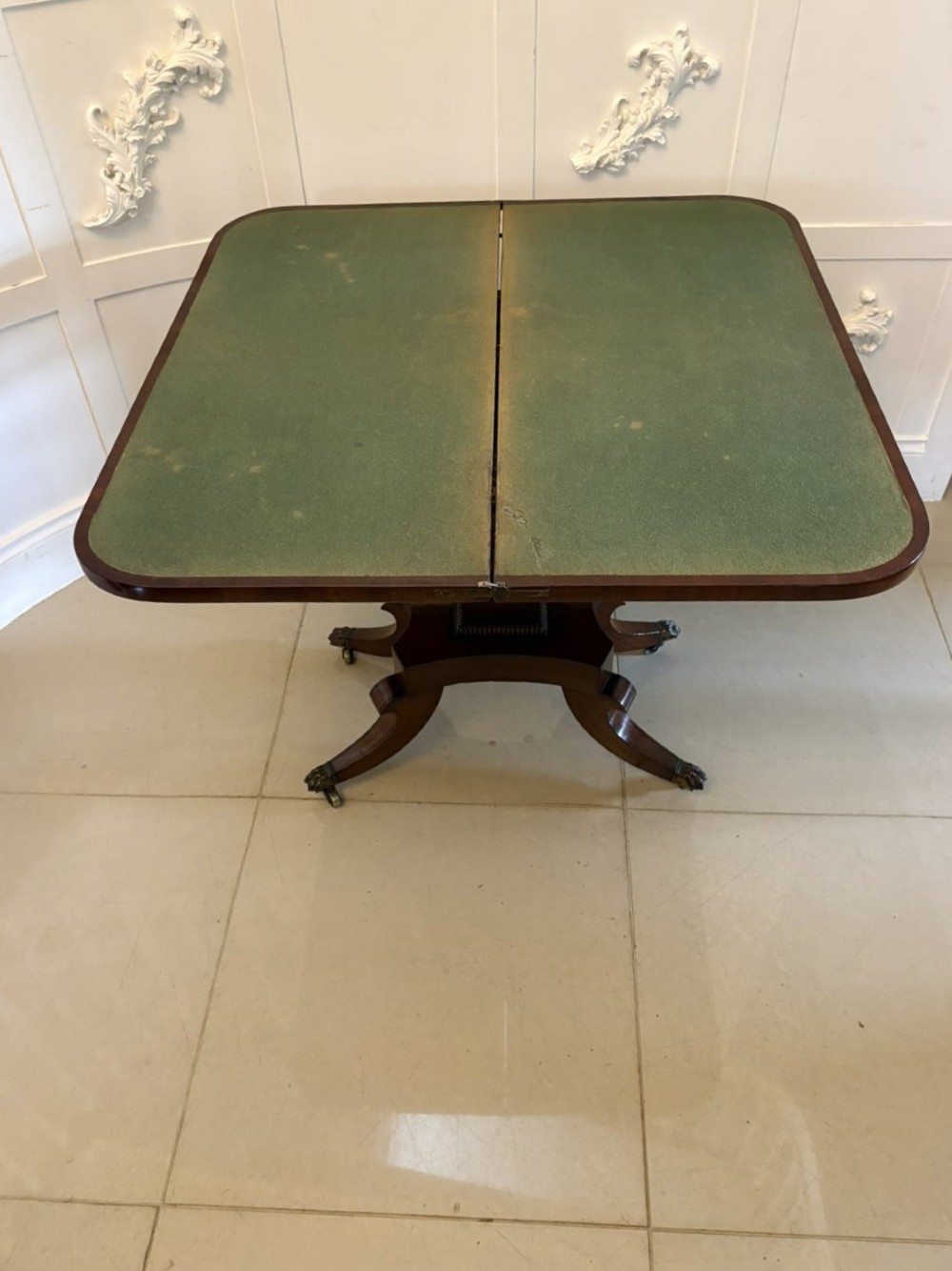 An antique Regency mahogany fold-over card table featuring brass marquetry inlay, a central shaped pedestal, and a splayed base with brass castors. View VI