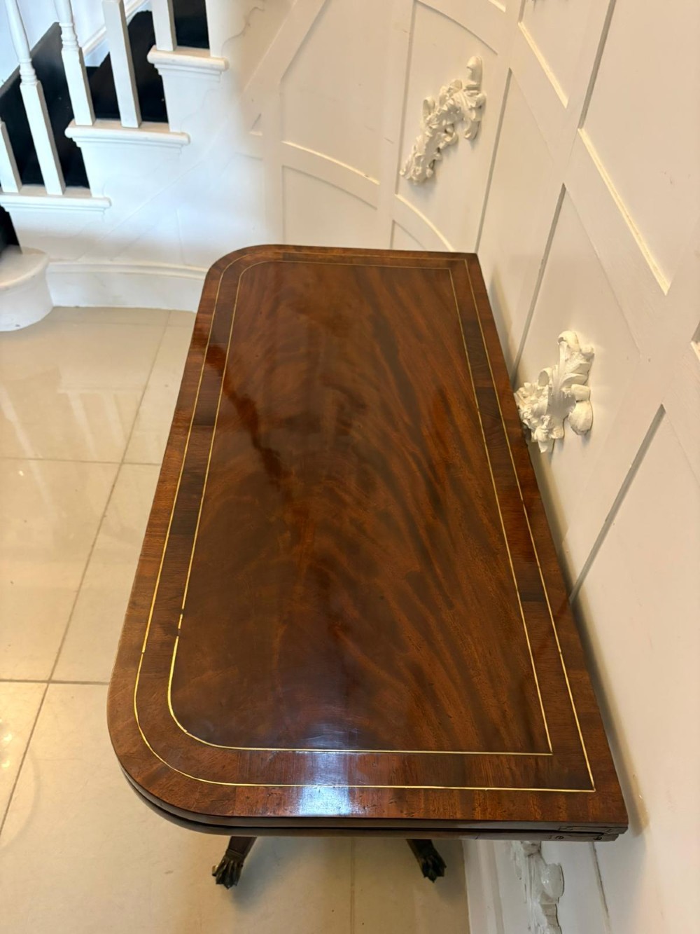 An antique Regency mahogany fold-over card table featuring brass marquetry inlay, a central shaped pedestal, and a splayed base with brass castors. View X