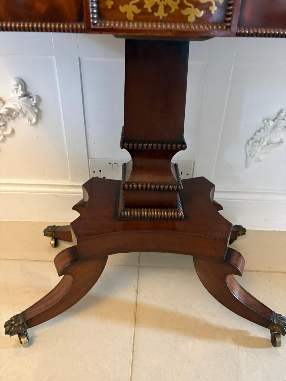 An antique Regency mahogany fold-over card table featuring brass marquetry inlay, a central shaped pedestal, and a splayed base with brass castors. View XIV