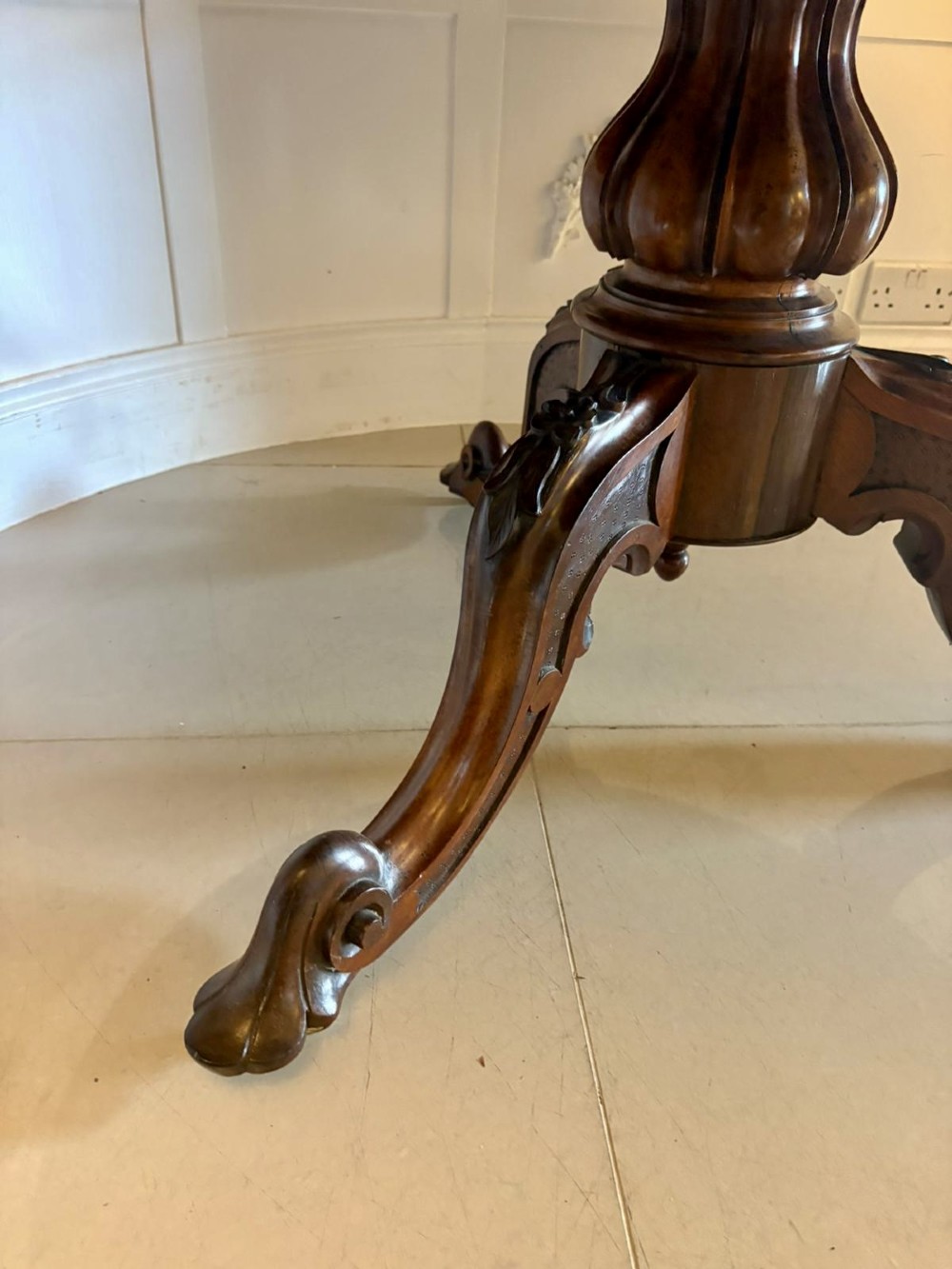 A Victorian circular rosewood dining table with a matched grain veneer top, shown tilted vertically on a carved pedestal base with scroll feet. View II