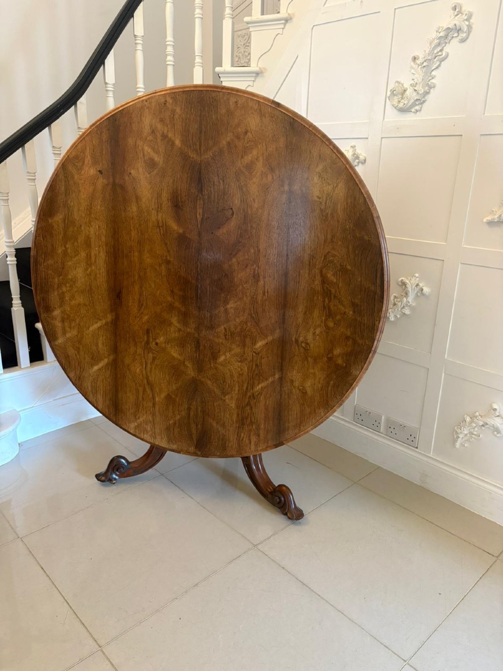 A Victorian circular rosewood dining table with a matched grain veneer top, shown tilted vertically on a carved pedestal base with scroll feet. View III