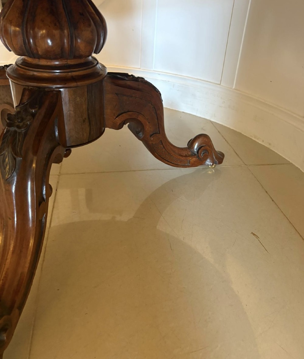 A Victorian circular rosewood dining table with a matched grain veneer top, shown tilted vertically on a carved pedestal base with scroll feet. View IV