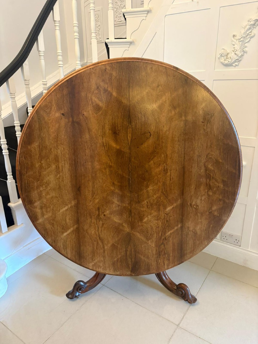 A Victorian circular rosewood dining table with a matched grain veneer top, shown tilted vertically on a carved pedestal base with scroll feet. View VIII