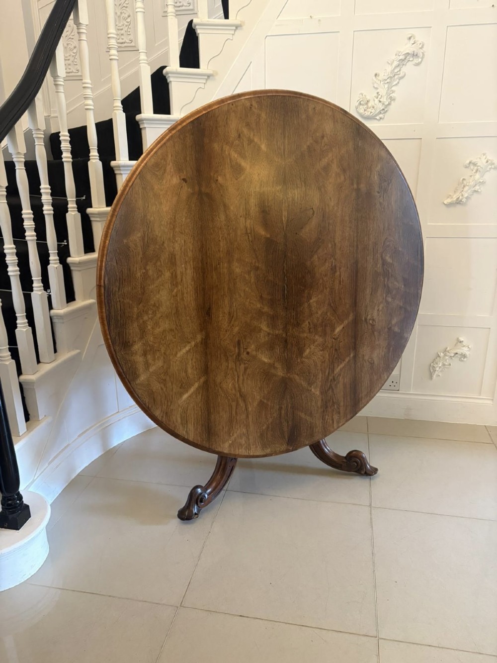 A Victorian circular rosewood dining table with a matched grain veneer top, shown tilted vertically on a carved pedestal base with scroll feet. View XI