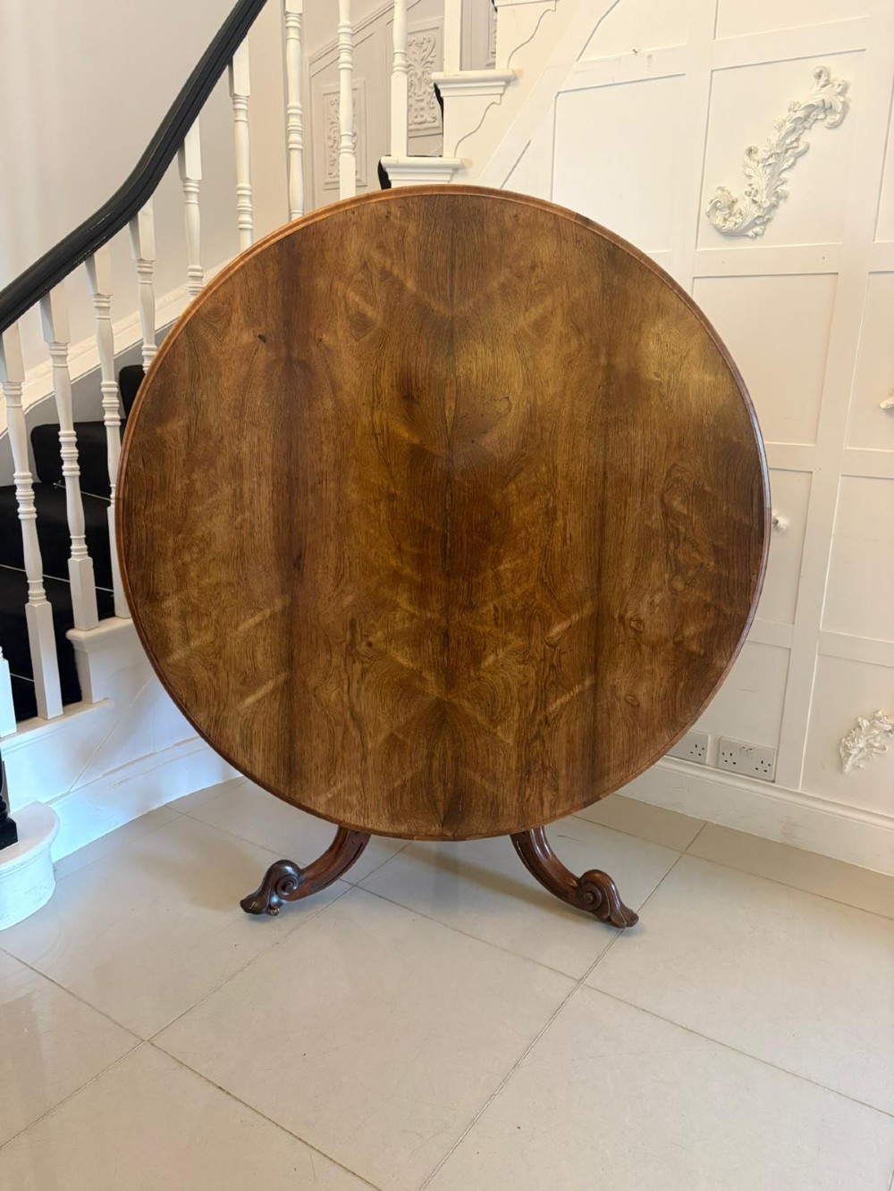 A Victorian circular rosewood dining table with a matched grain veneer top, shown tilted vertically on a carved pedestal base with scroll feet.