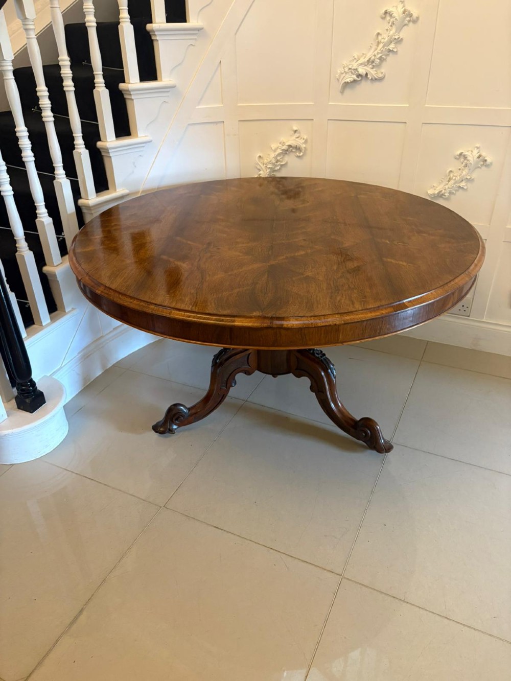 A Victorian circular rosewood dining table with a matched grain veneer top, shown tilted vertically on a carved pedestal base with scroll feet. View XII