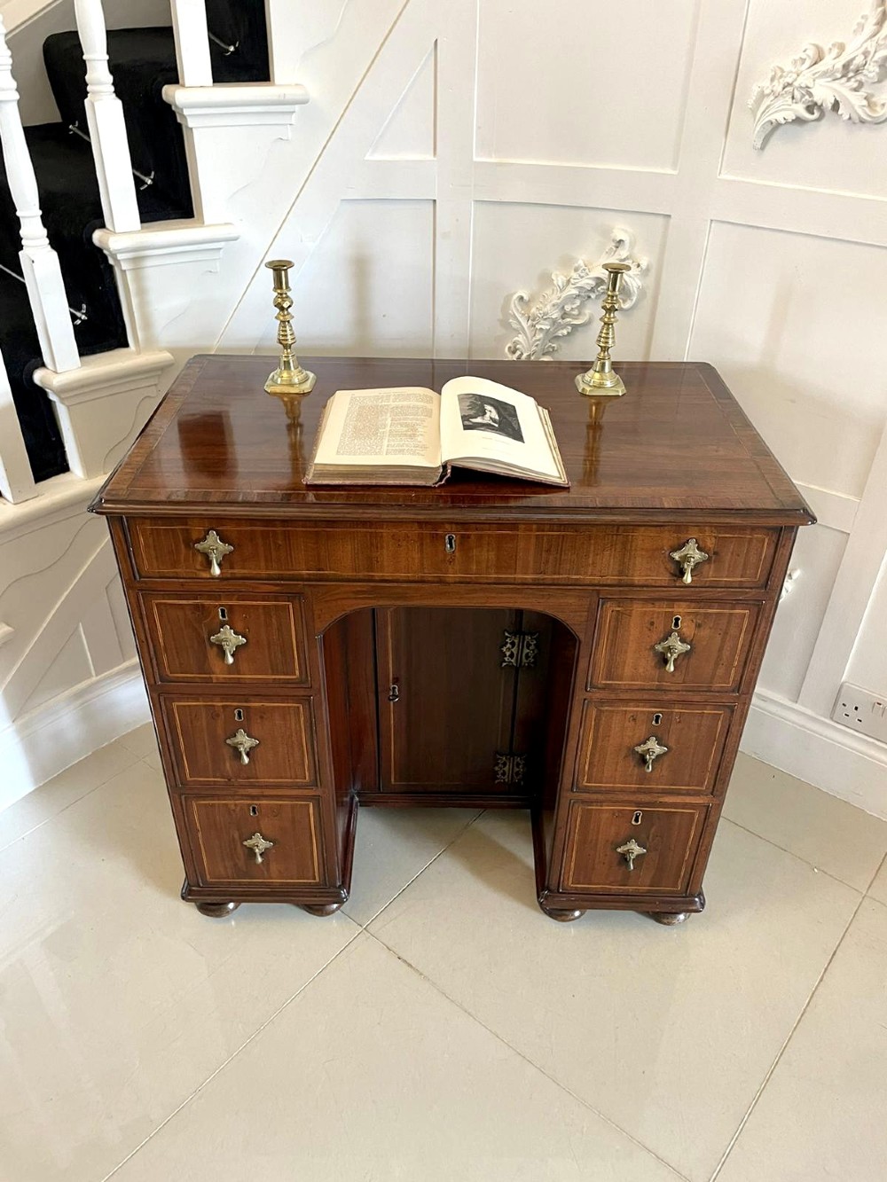 An antique George III walnut kneehole desk featuring crossbanded veneer, brass drop handles, a long frieze drawer, and six pedestal drawers flanking a recessed central cupboard. View III