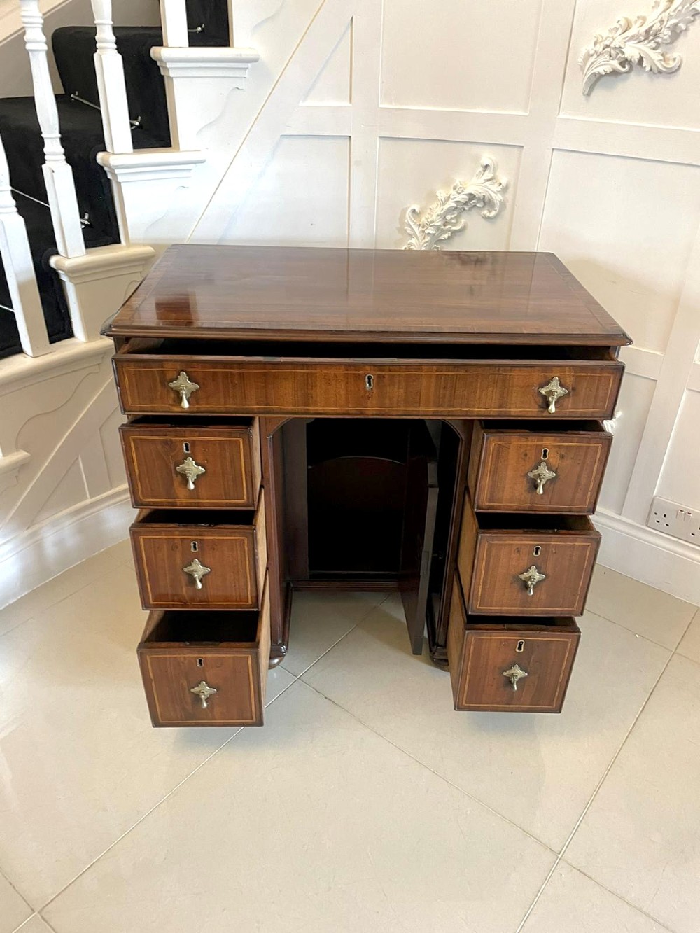 An antique George III walnut kneehole desk featuring crossbanded veneer, brass drop handles, a long frieze drawer, and six pedestal drawers flanking a recessed central cupboard. View IV