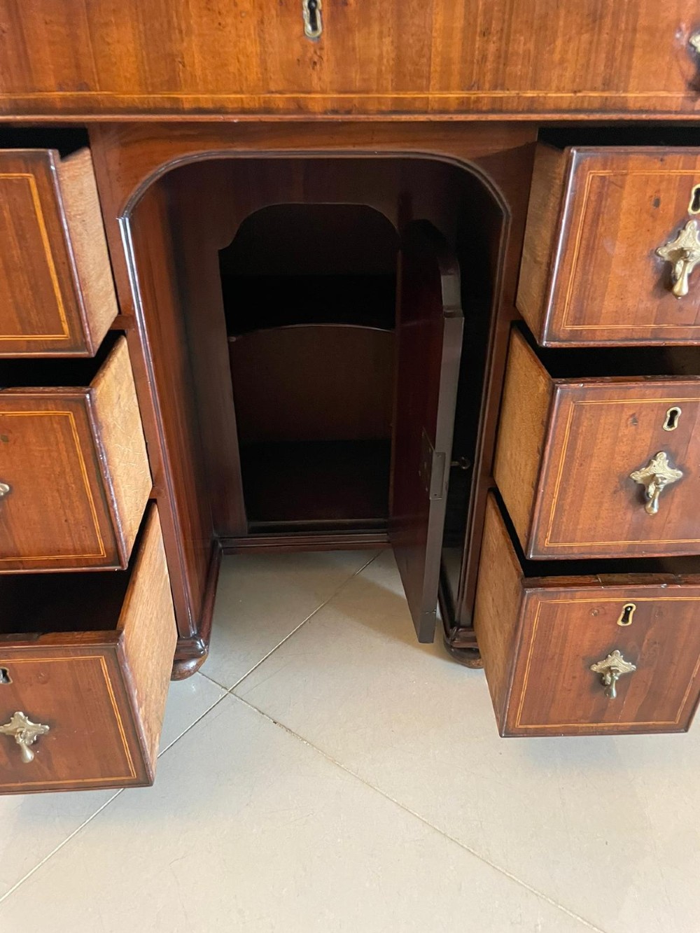 An antique George III walnut kneehole desk featuring crossbanded veneer, brass drop handles, a long frieze drawer, and six pedestal drawers flanking a recessed central cupboard. View V