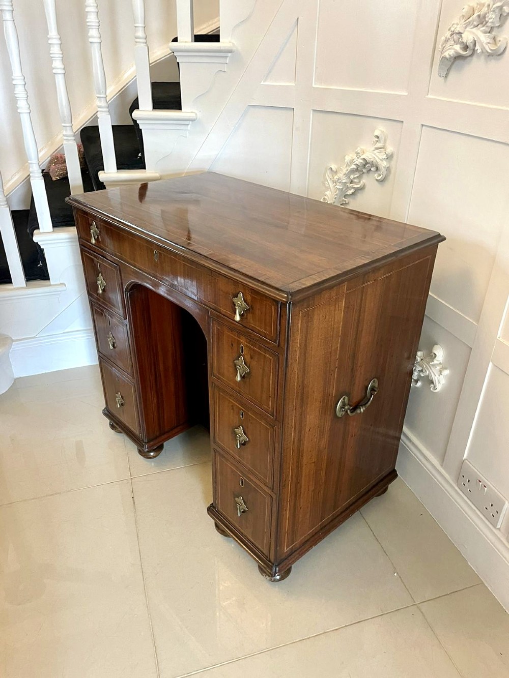 An antique George III walnut kneehole desk featuring crossbanded veneer, brass drop handles, a long frieze drawer, and six pedestal drawers flanking a recessed central cupboard. View VIII