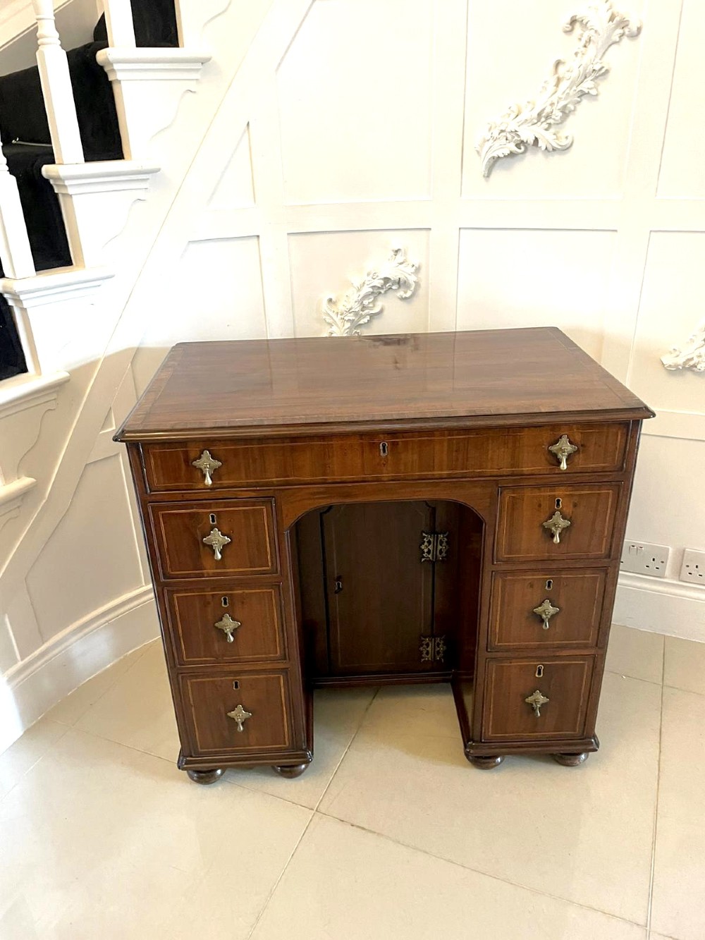 An antique George III walnut kneehole desk featuring crossbanded veneer, brass drop handles, a long frieze drawer, and six pedestal drawers flanking a recessed central cupboard. View IX
