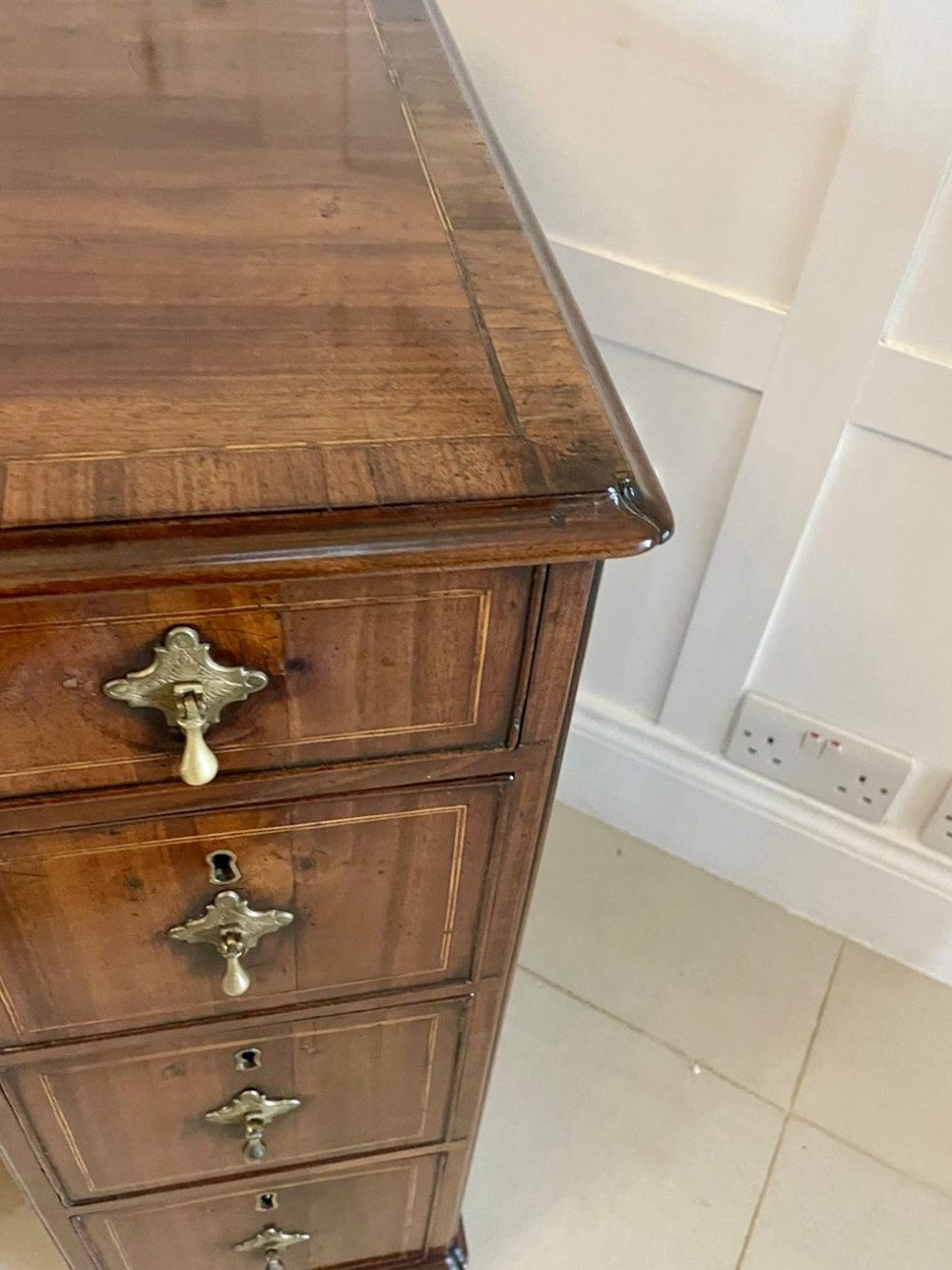 An antique George III walnut kneehole desk featuring crossbanded veneer, brass drop handles, a long frieze drawer, and six pedestal drawers flanking a recessed central cupboard. View X