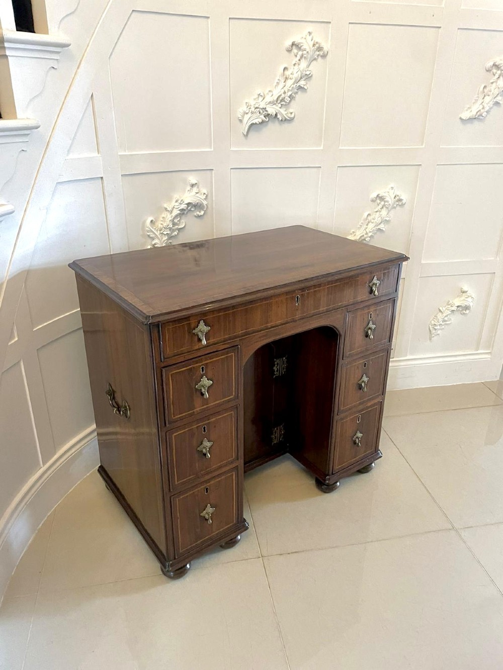 An antique George III walnut kneehole desk featuring crossbanded veneer, brass drop handles, a long frieze drawer, and six pedestal drawers flanking a recessed central cupboard. View XII