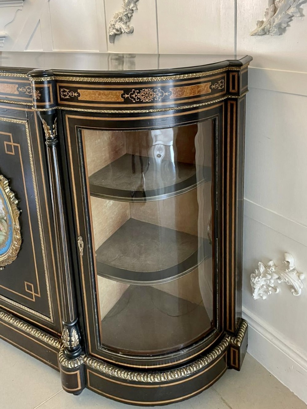 An ebonised nineteenth-century French credenza featuring amboyna wood inlays, gilt-bronze mounts, curved glass door cabinets, and a central painted porcelain plaque. View X