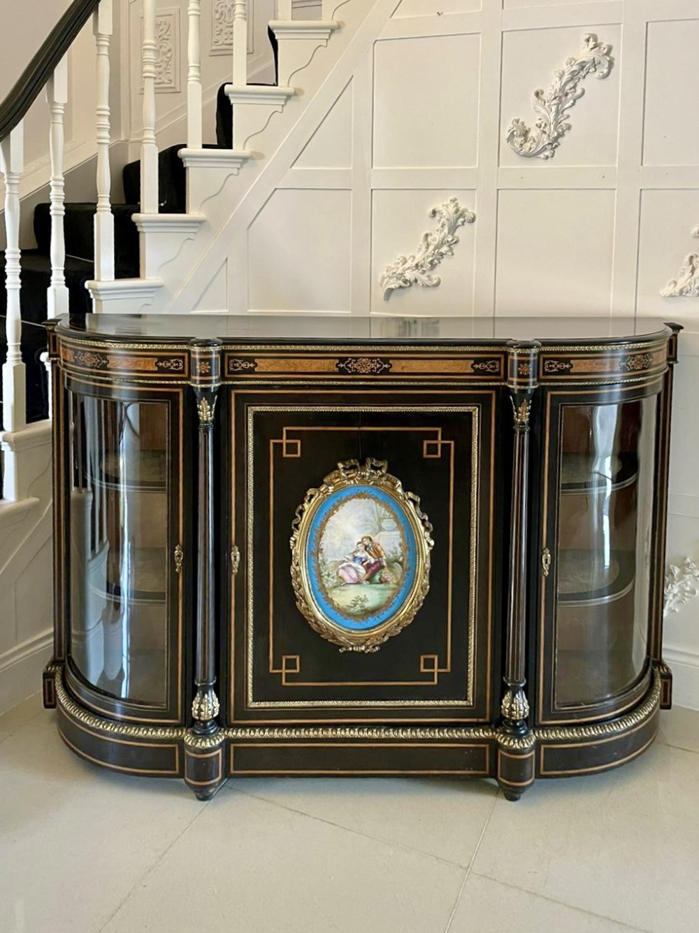 An ebonised nineteenth-century French credenza featuring amboyna wood inlays, gilt-bronze mounts, curved glass door cabinets, and a central painted porcelain plaque.