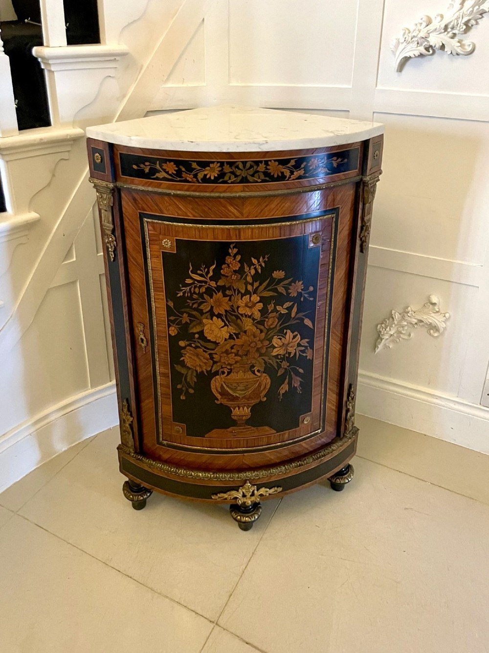 A French Louis XVI style corner cabinet featuring a bow-front door with floral wood marquetry inlay, gilt bronze mounts, and a fitted white marble top.