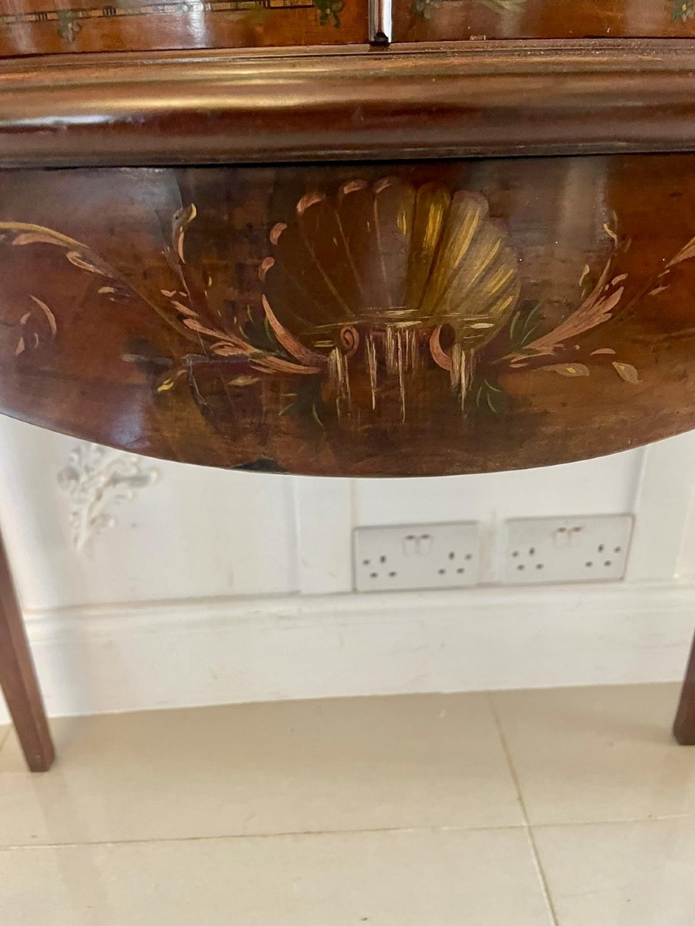 An antique mahogany display cabinet featuring a swan-neck pediment, glazed twin doors, hand-painted floral decoration, and slender tapered legs. View III